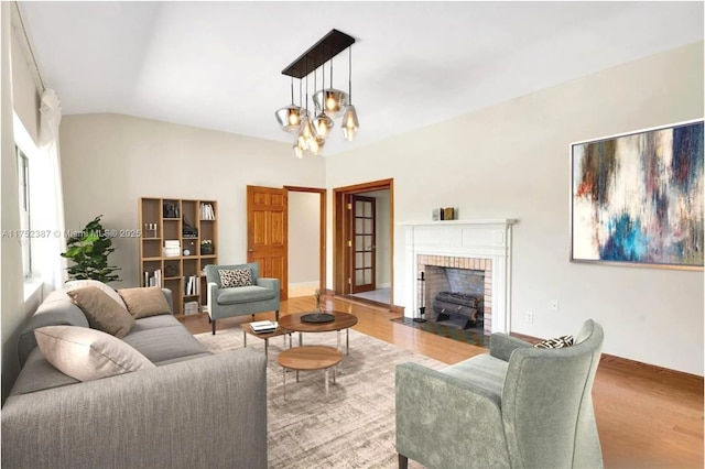 living room with lofted ceiling, a fireplace, a notable chandelier, and wood finished floors