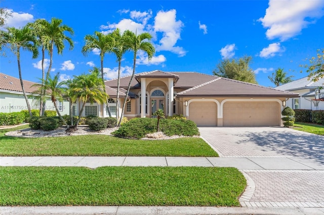 mediterranean / spanish-style home with a garage, a tiled roof, decorative driveway, stucco siding, and a front yard