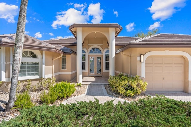 view of exterior entry with a garage, french doors, a tiled roof, and stucco siding