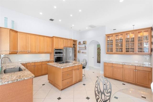 kitchen featuring arched walkways, stainless steel appliances, glass insert cabinets, a kitchen island with sink, and a sink