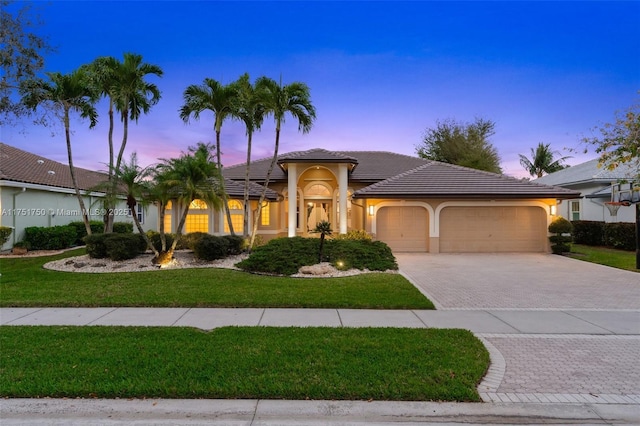 mediterranean / spanish-style house featuring a garage, a tiled roof, decorative driveway, a yard, and stucco siding