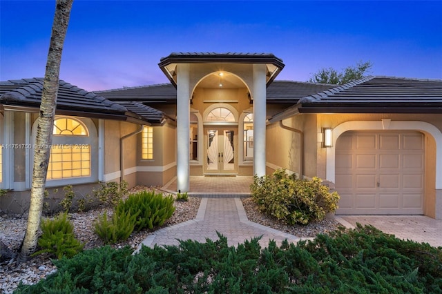 view of exterior entry featuring an attached garage, a tiled roof, and stucco siding