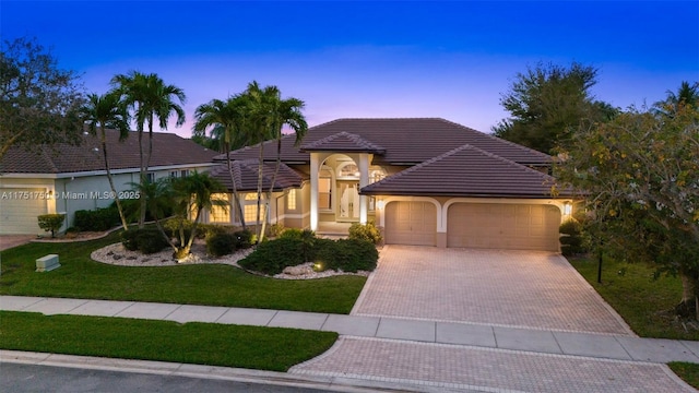 view of front of house with decorative driveway, a yard, stucco siding, a garage, and a tiled roof