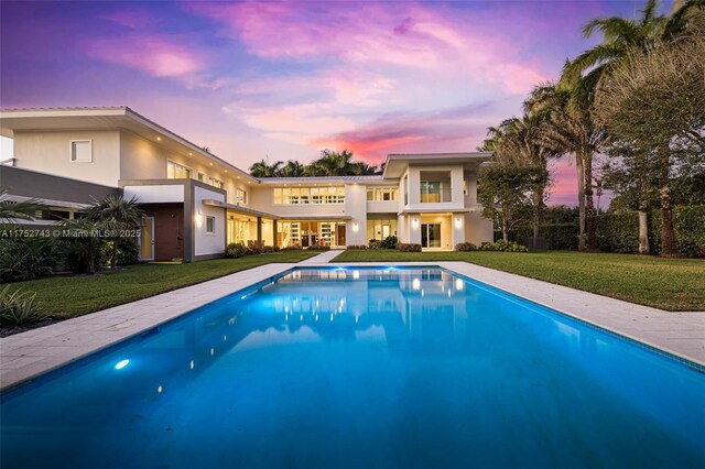 6080 SW 88th St, Pinecrest, FL 33156 - back of house at dusk featuring an outdoor pool, a lawn, and stucco siding