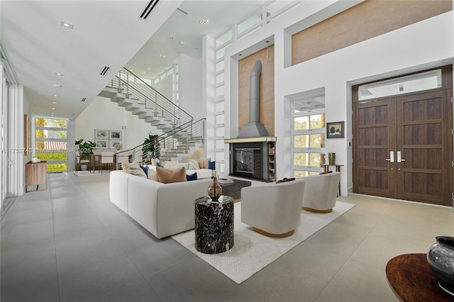 living area featuring a towering ceiling, a wood stove, visible vents, and stairway