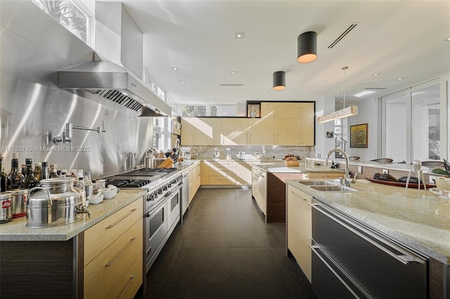 kitchen featuring tasteful backsplash, range with two ovens, wall chimney range hood, pendant lighting, and a sink