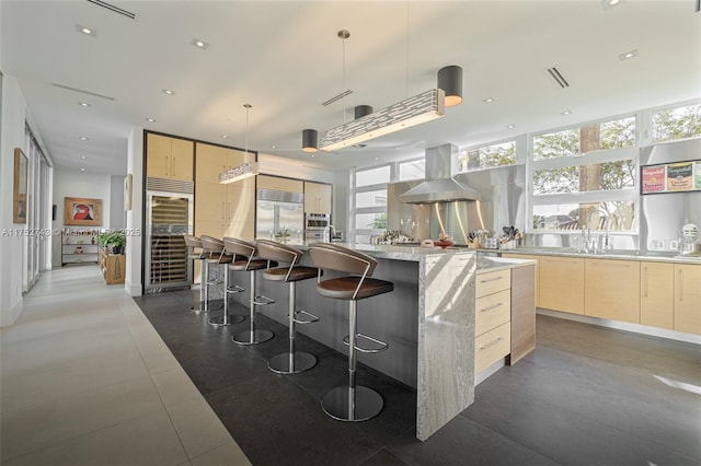 kitchen with a center island, hanging light fixtures, island exhaust hood, light brown cabinetry, and built in fridge