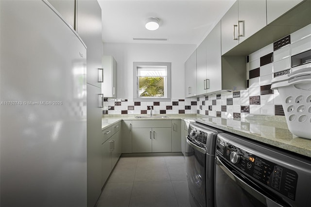 kitchen featuring washer and clothes dryer, light tile patterned floors, tasteful backsplash, a sink, and light stone countertops