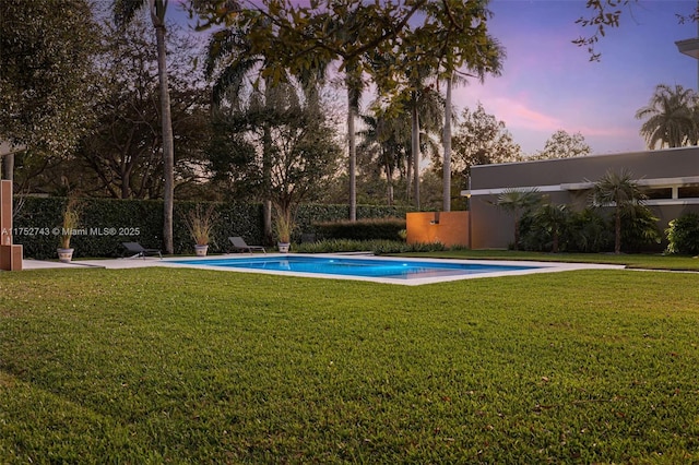 pool at dusk featuring a fenced in pool and a lawn