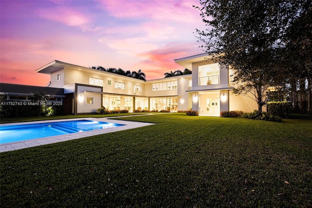 rear view of property featuring a yard, an outdoor pool, and stucco siding