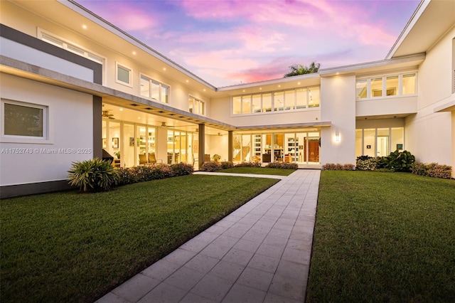 back of property at dusk with a yard and stucco siding