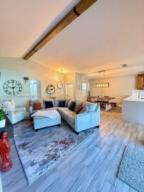 living room with arched walkways, visible vents, wood finish floors, and lofted ceiling with beams