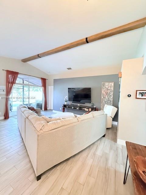 living area featuring vaulted ceiling with beams, light wood finished floors, and baseboards