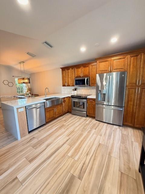 kitchen featuring visible vents, brown cabinets, a peninsula, stainless steel appliances, and a sink