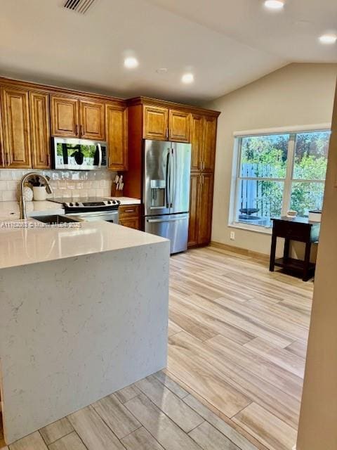 kitchen with wood finish floors, brown cabinets, stainless steel appliances, lofted ceiling, and backsplash