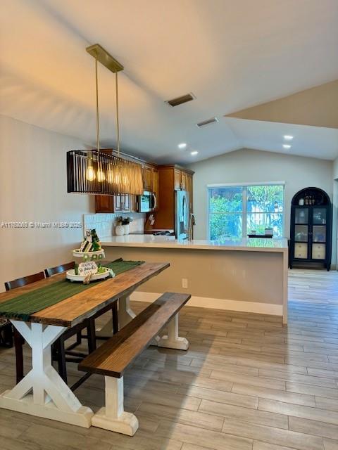 dining space featuring baseboards, visible vents, vaulted ceiling, and light wood finished floors