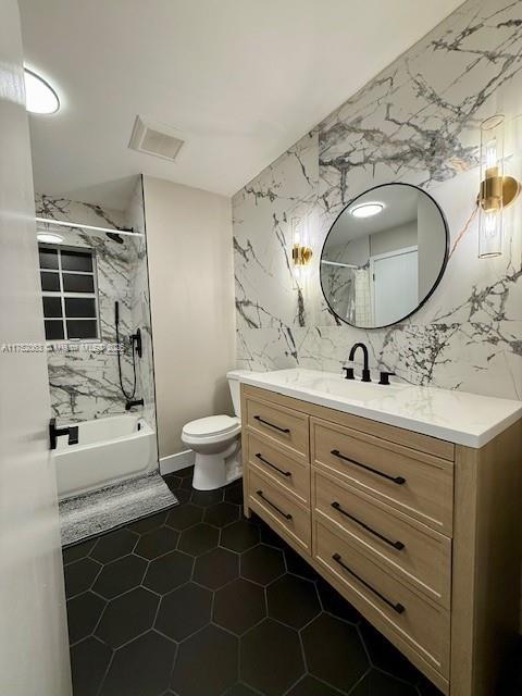 bathroom with toilet, visible vents, vanity, tile walls, and washtub / shower combination