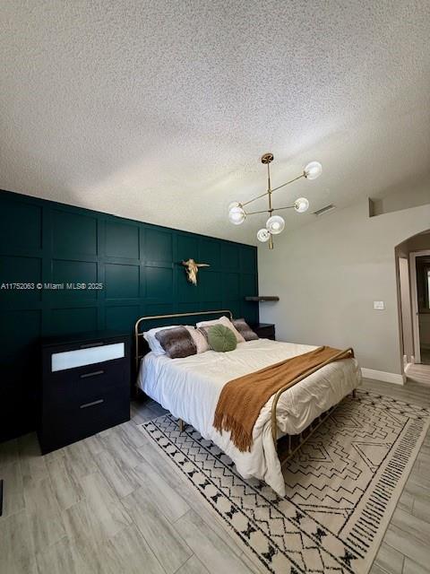 bedroom with visible vents, a decorative wall, a textured ceiling, light wood-type flooring, and baseboards