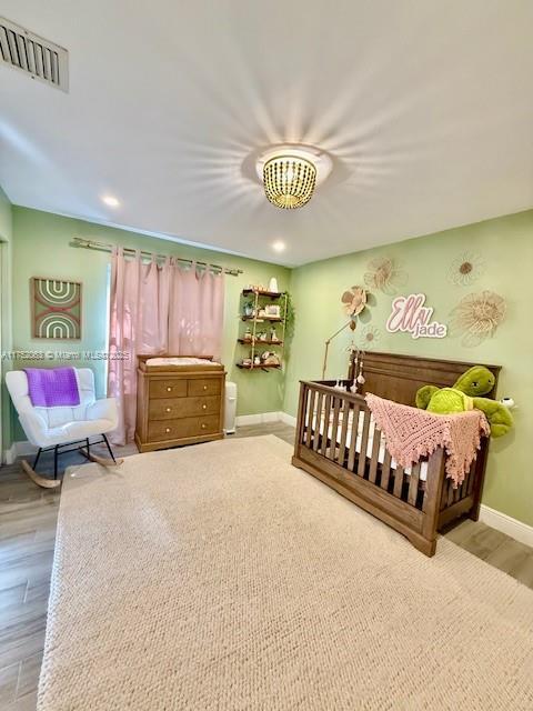 bedroom with wood finished floors, visible vents, and baseboards