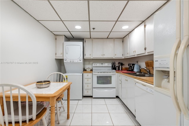 kitchen with white appliances, stacked washer / dryer, a sink, white cabinetry, and light countertops