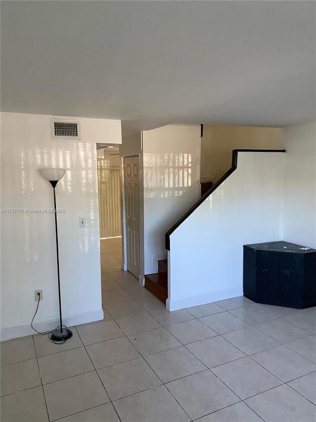 empty room featuring stairway, light tile patterned floors, and visible vents