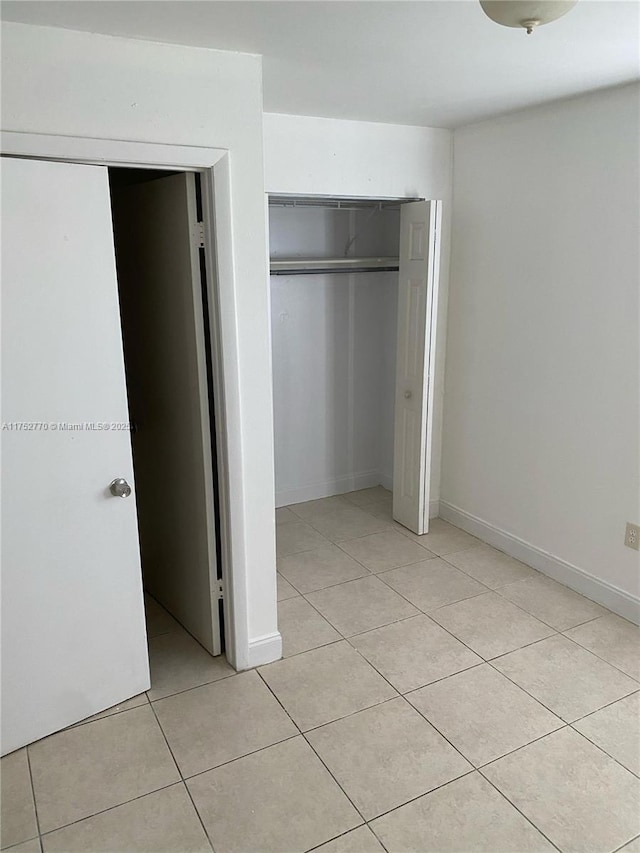 unfurnished bedroom featuring light tile patterned floors, baseboards, and a closet