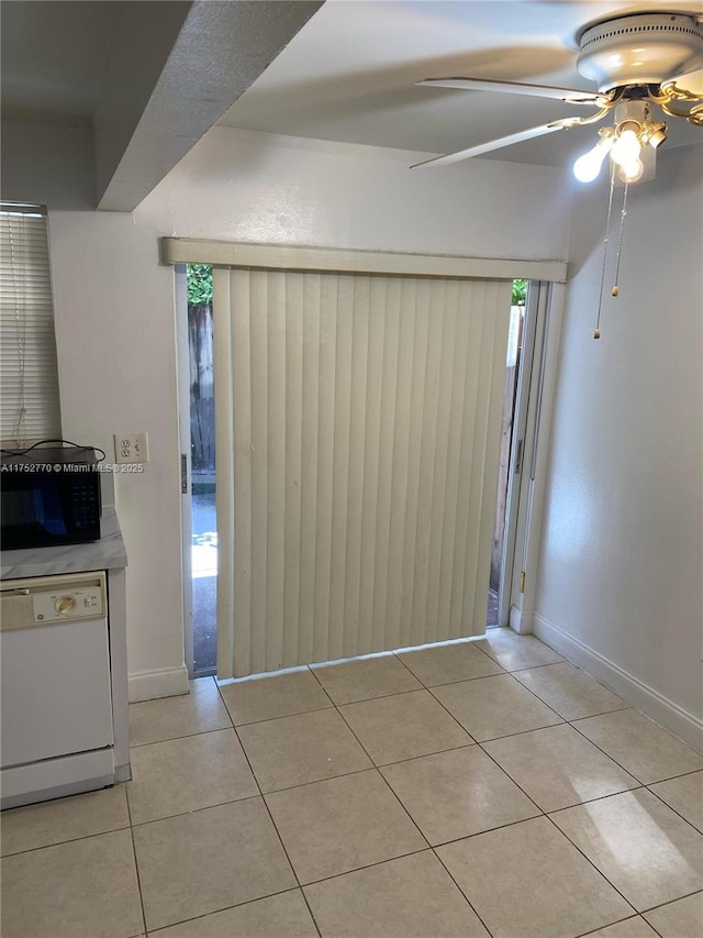 empty room featuring light tile patterned floors, baseboards, a wealth of natural light, and a ceiling fan