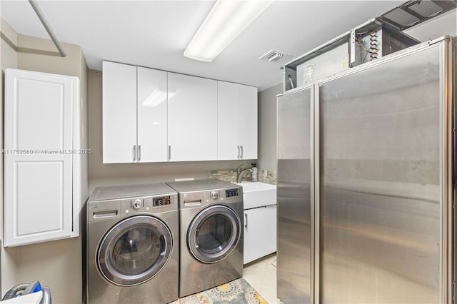 washroom with visible vents, washing machine and clothes dryer, a sink, and cabinet space