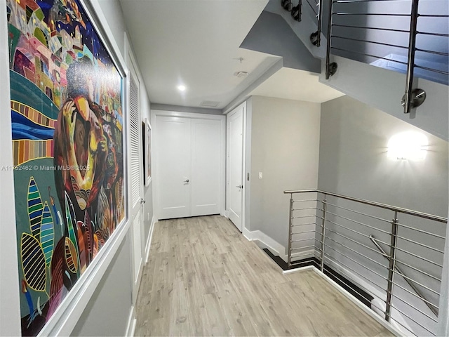 hall with an upstairs landing, baseboards, and light wood finished floors