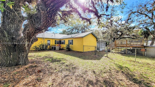 back of property featuring central air condition unit, fence, metal roof, and a lawn