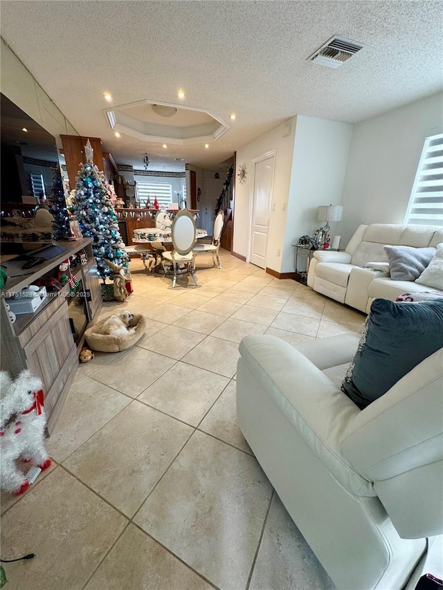 living room with a textured ceiling, light tile patterned floors, a raised ceiling, and visible vents