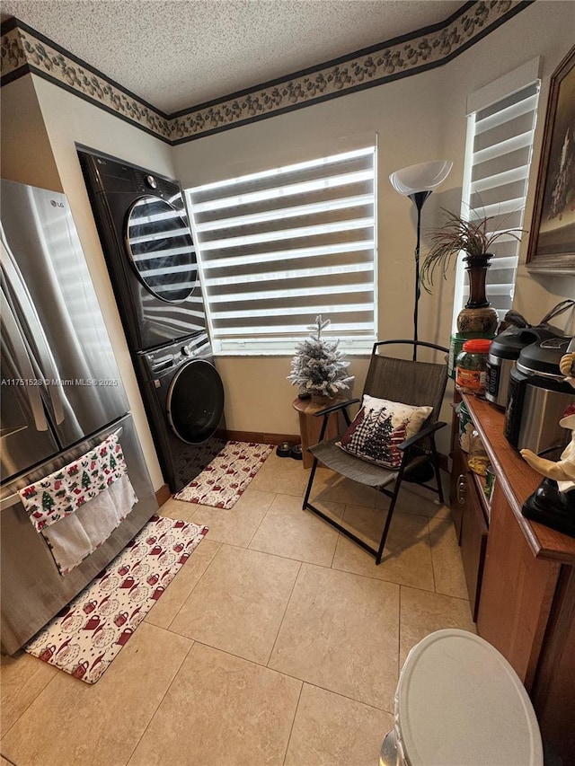 clothes washing area featuring laundry area, light tile patterned flooring, a textured ceiling, and stacked washing maching and dryer