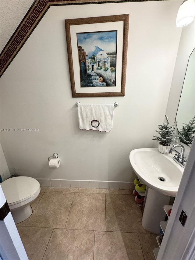 bathroom featuring toilet, baseboards, a sink, and tile patterned floors