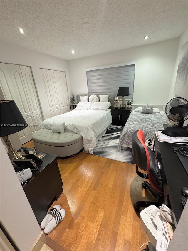 bedroom with a textured ceiling, light wood finished floors, recessed lighting, and multiple closets