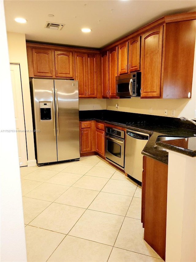 kitchen featuring light tile patterned floors, visible vents, appliances with stainless steel finishes, a sink, and dark stone counters