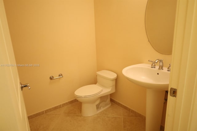 half bathroom featuring a sink, tile patterned flooring, toilet, and baseboards