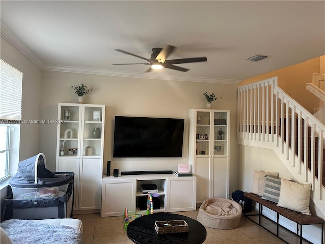 living area with a ceiling fan, tile patterned floors, crown molding, and stairs