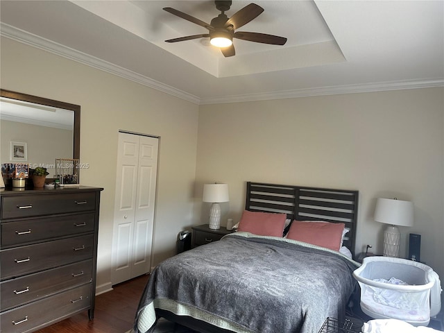 bedroom featuring ceiling fan, dark wood-style flooring, a closet, a tray ceiling, and crown molding