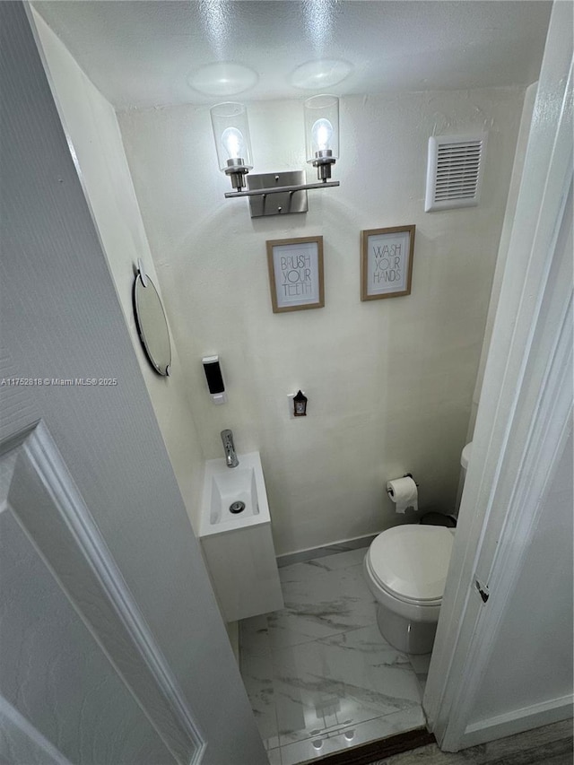 half bathroom featuring toilet, marble look tile flooring, and baseboards