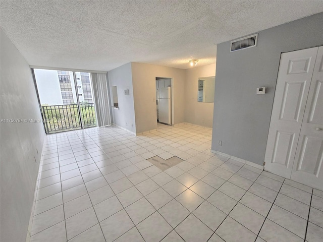 empty room featuring expansive windows, visible vents, a textured ceiling, and light tile patterned flooring