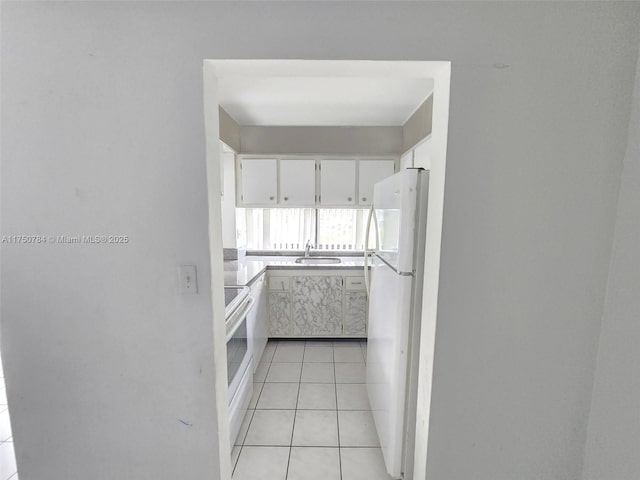 kitchen featuring light tile patterned floors, light countertops, white cabinetry, a sink, and white appliances