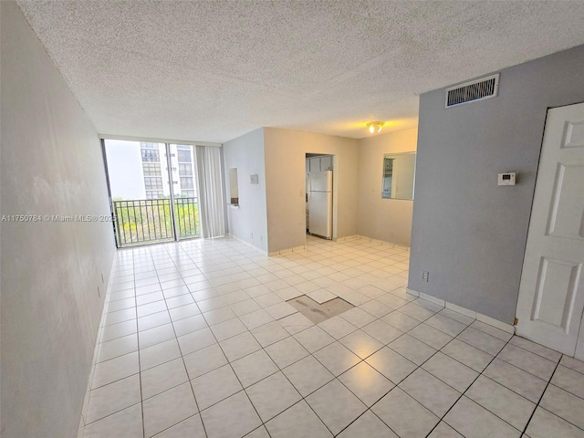 spare room with a textured ceiling, a wall of windows, light tile patterned flooring, and visible vents