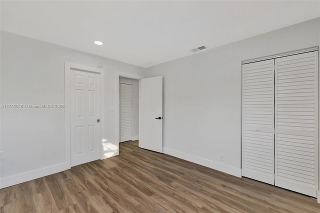 unfurnished bedroom with recessed lighting, a closet, visible vents, wood finished floors, and baseboards