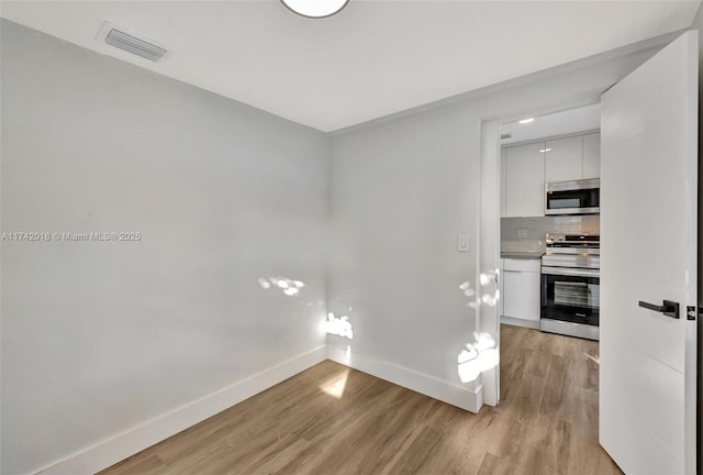 empty room featuring light wood-type flooring, visible vents, and baseboards