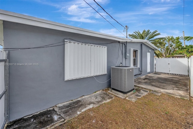 view of home's exterior with a gate, stucco siding, fence, and central air condition unit