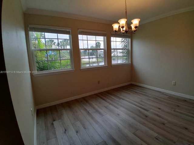 spare room with crown molding, baseboards, a chandelier, and wood finished floors