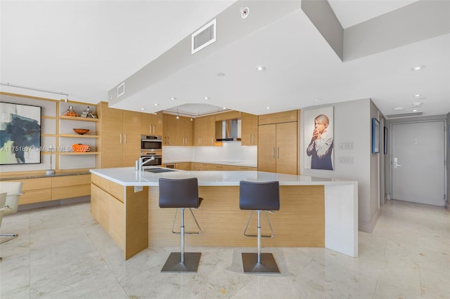 kitchen featuring a spacious island, visible vents, light countertops, wall chimney range hood, and modern cabinets