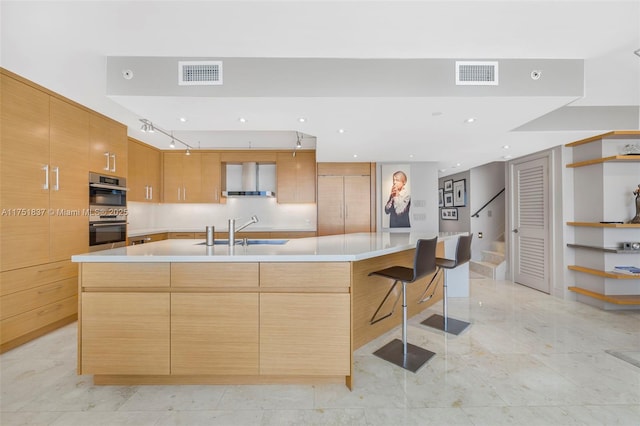 kitchen featuring wall chimney range hood, modern cabinets, visible vents, and a sink