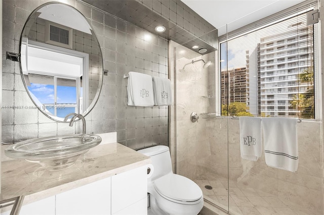 full bath with toilet, tiled shower, vanity, and tile walls