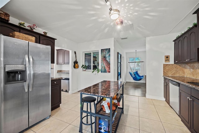5801 NE 3rd Ave, Oakland Park, FL 33334 - kitchen with light tile patterned floors, dark brown cabinetry, stainless steel appliances, tasteful backsplash, and dark stone countertops